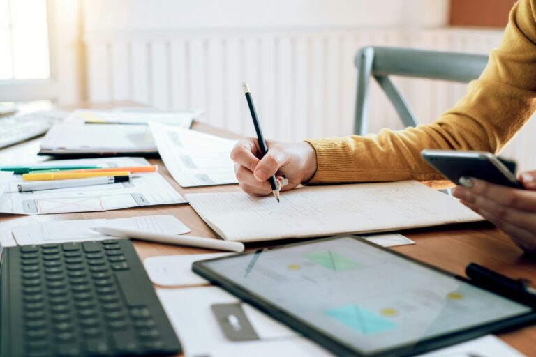 A designer sketching wireframes in a notebook beside a tablet and phone