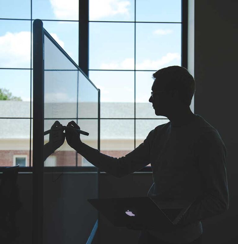 A silhouetted person writing on a glass board