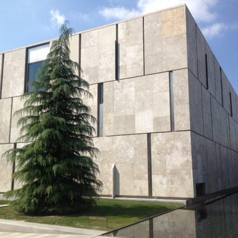 A modern stone building with an evergreen tree out front