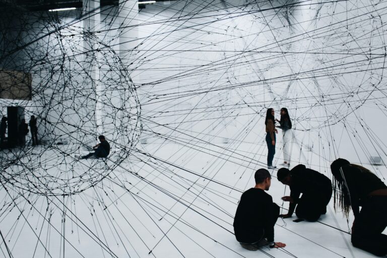 People inside an art installation of black strings connecting across a white room